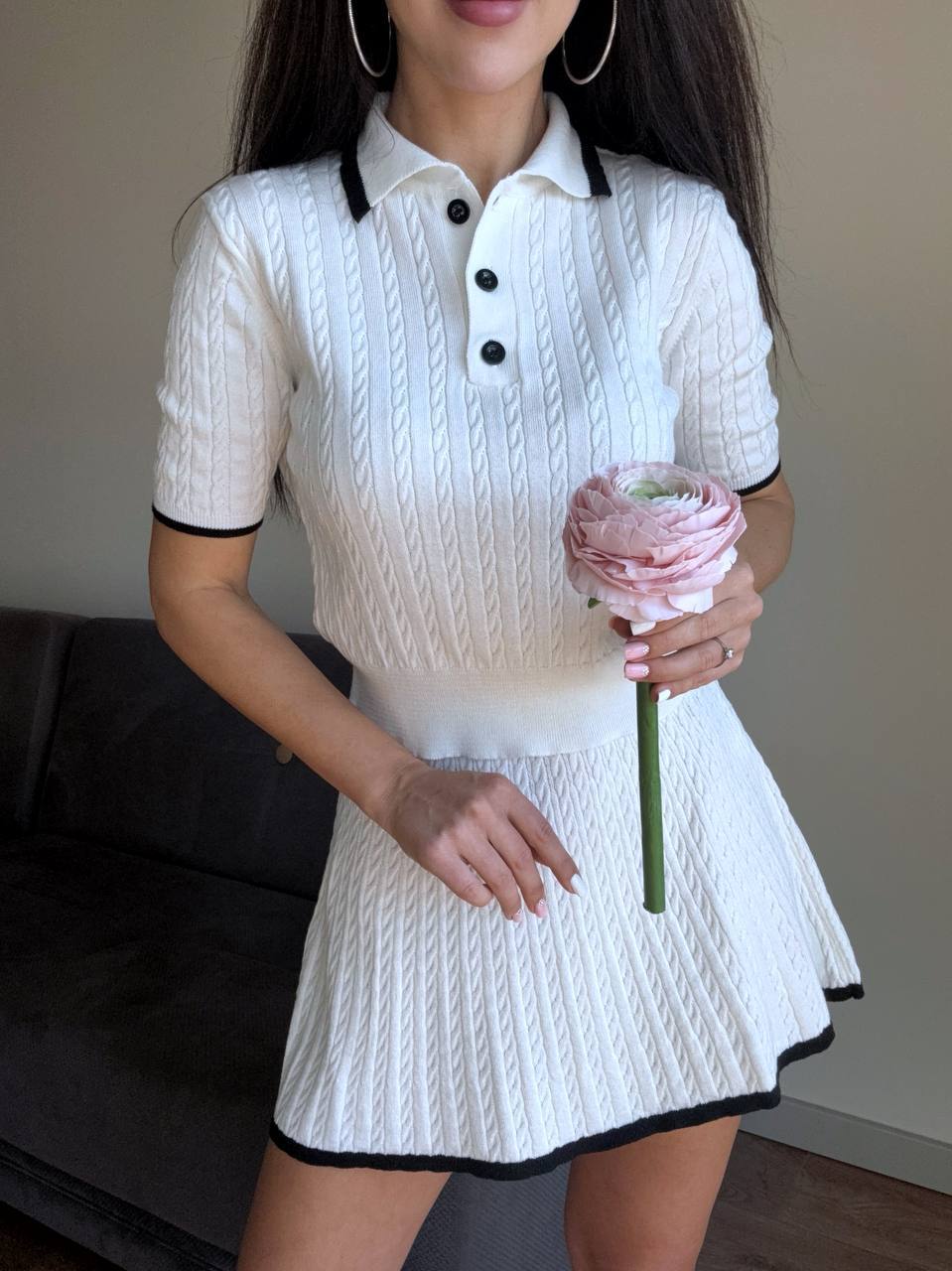 Person wearing a white dress with black trim holding a pink flower.