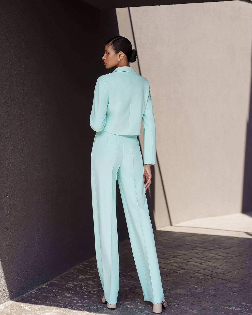 Woman in a light blue suit standing against a dark wall with a neutral background