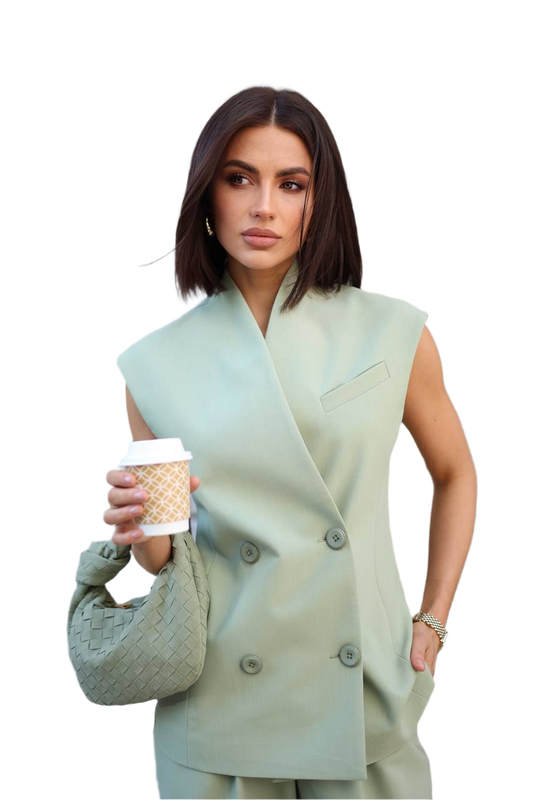 Woman wearing a light green sleeveless blazer holding a coffee cup on a white background