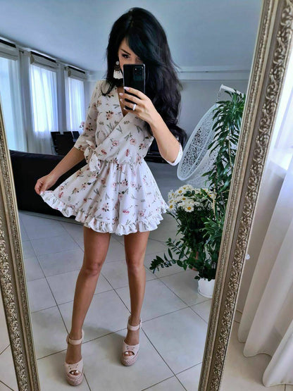 Woman taking a mirror selfie wearing a floral dress in a room with a decorative mirror.