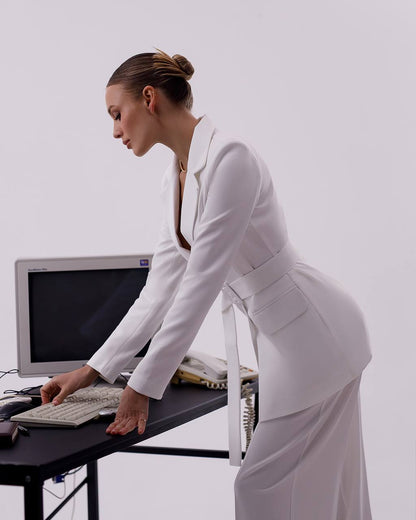 Woman in a white outfit using a computer on a desk against a plain background