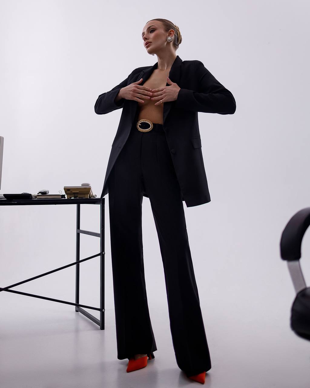 Person wearing a black suit with a belt, standing in a minimalistic setting.
