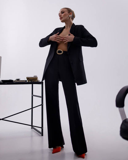 Person wearing a black suit with a belt, standing in a minimalistic setting.
