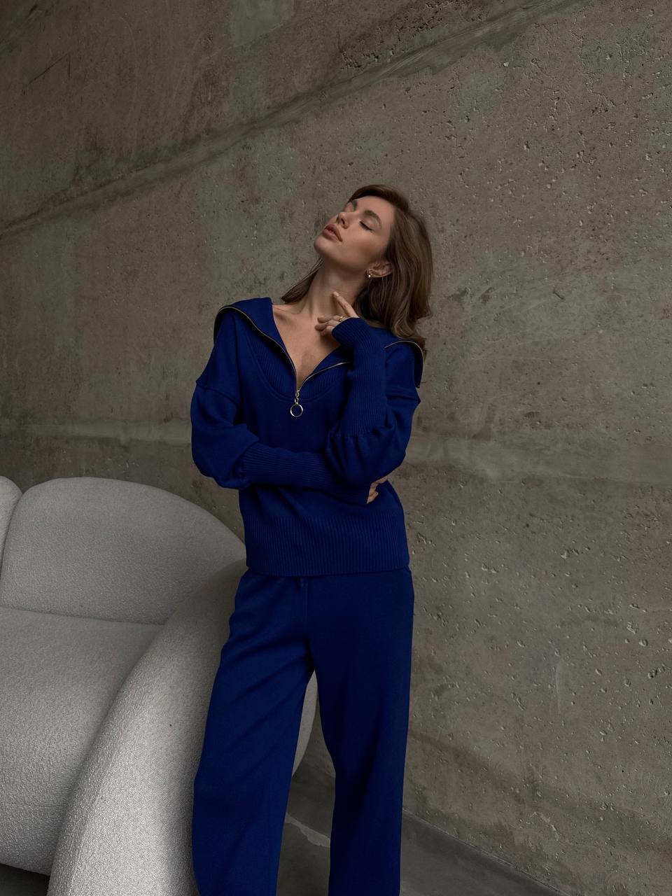 Woman in a blue outfit standing against a textured wall.