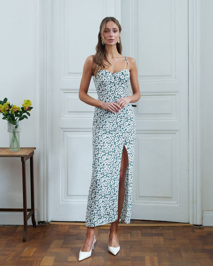 Woman in a floral dress standing in a room with wooden flooring and white walls.