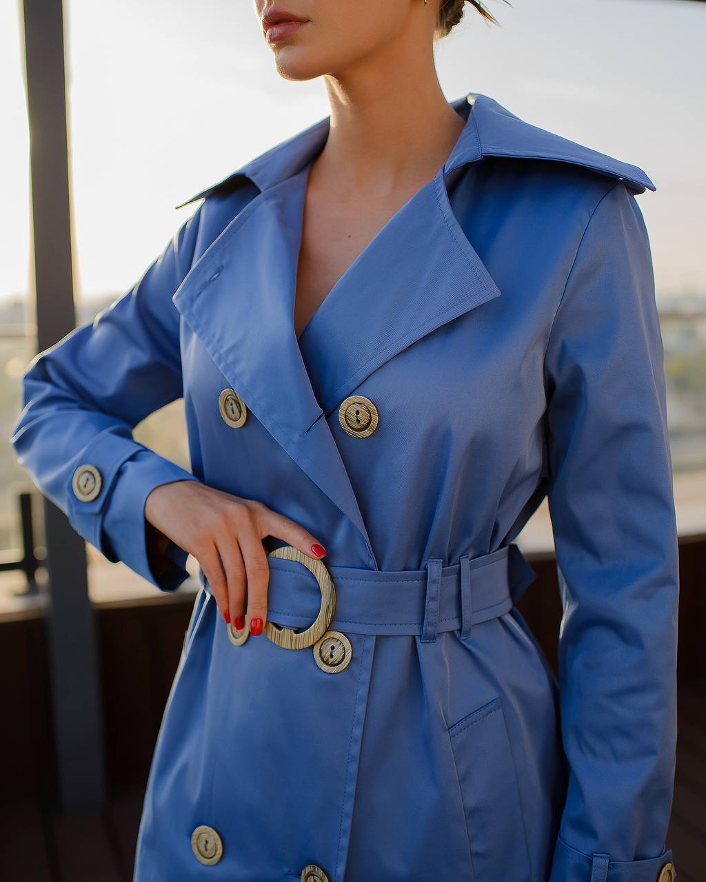Blue trench coat with gold buttons worn by a person, blurred background