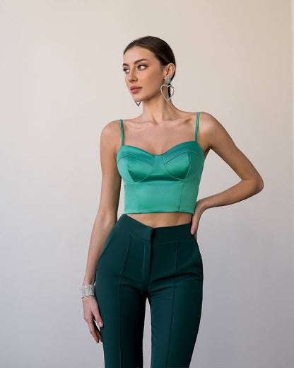 Woman wearing a green top and dark green pants against a plain background
