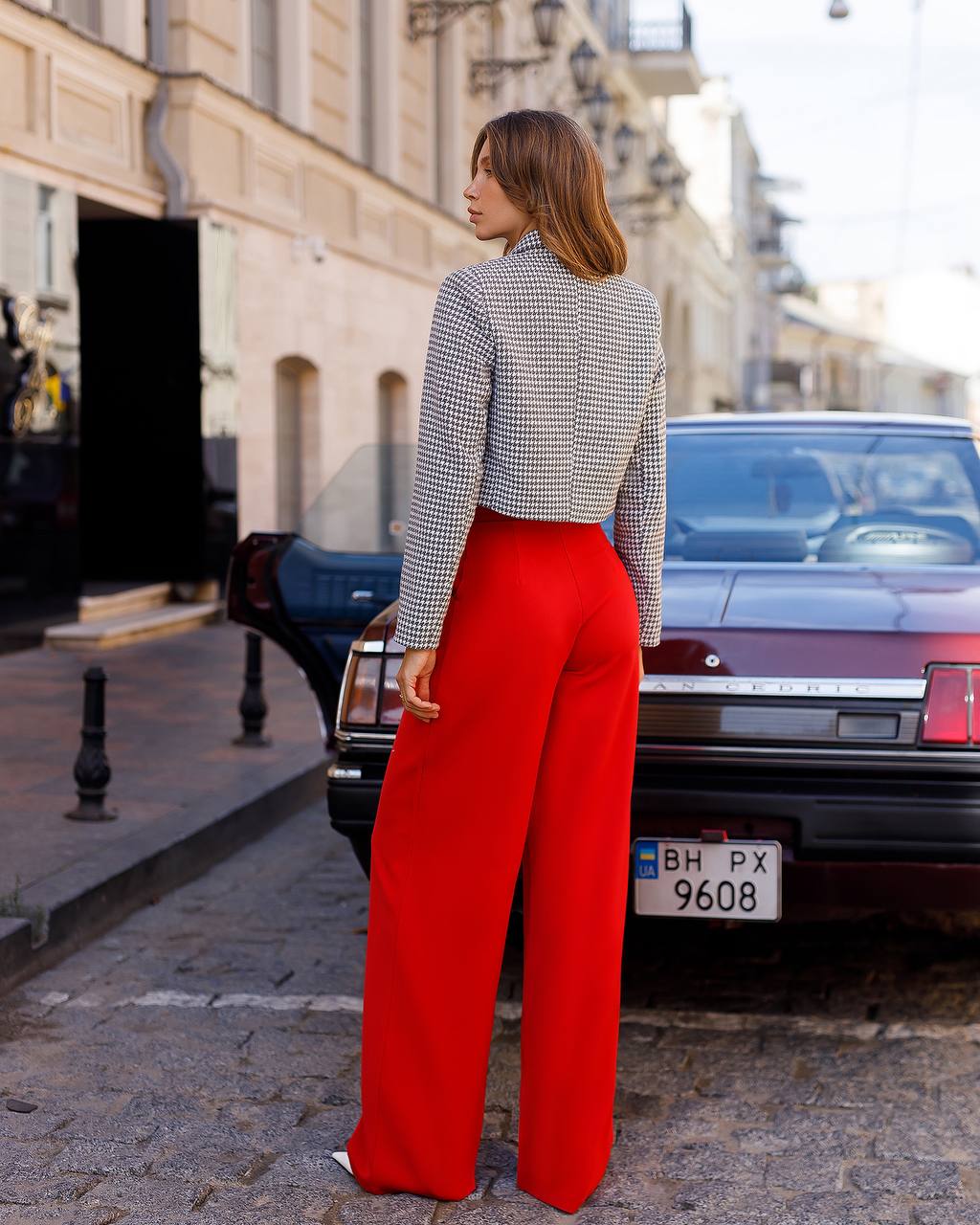 Woman wearing a patterned top and red pants standing on a street.