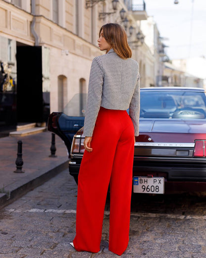 Woman wearing a patterned top and red pants standing on a street.