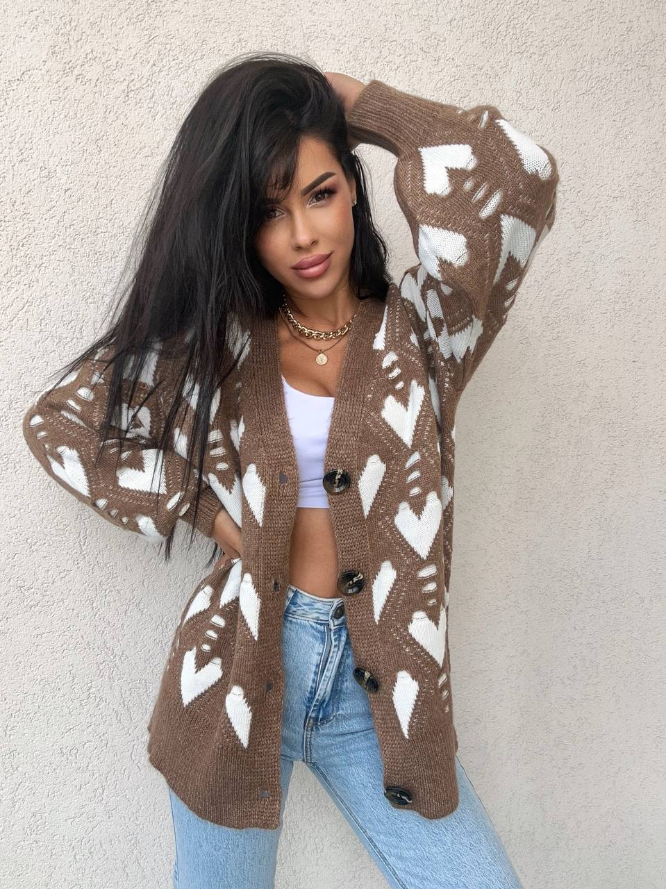 Woman wearing a brown cardigan with white patterns against a beige wall