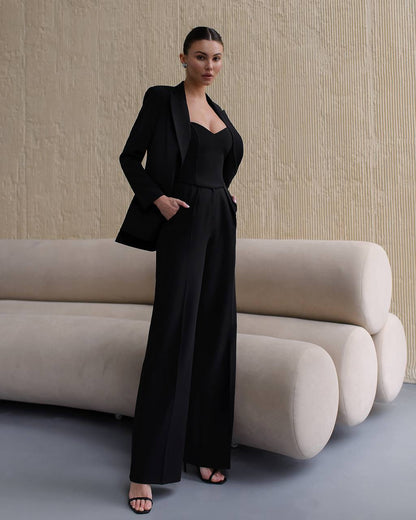 Woman in a black suit standing in front of a beige textured wall with a modern sofa.