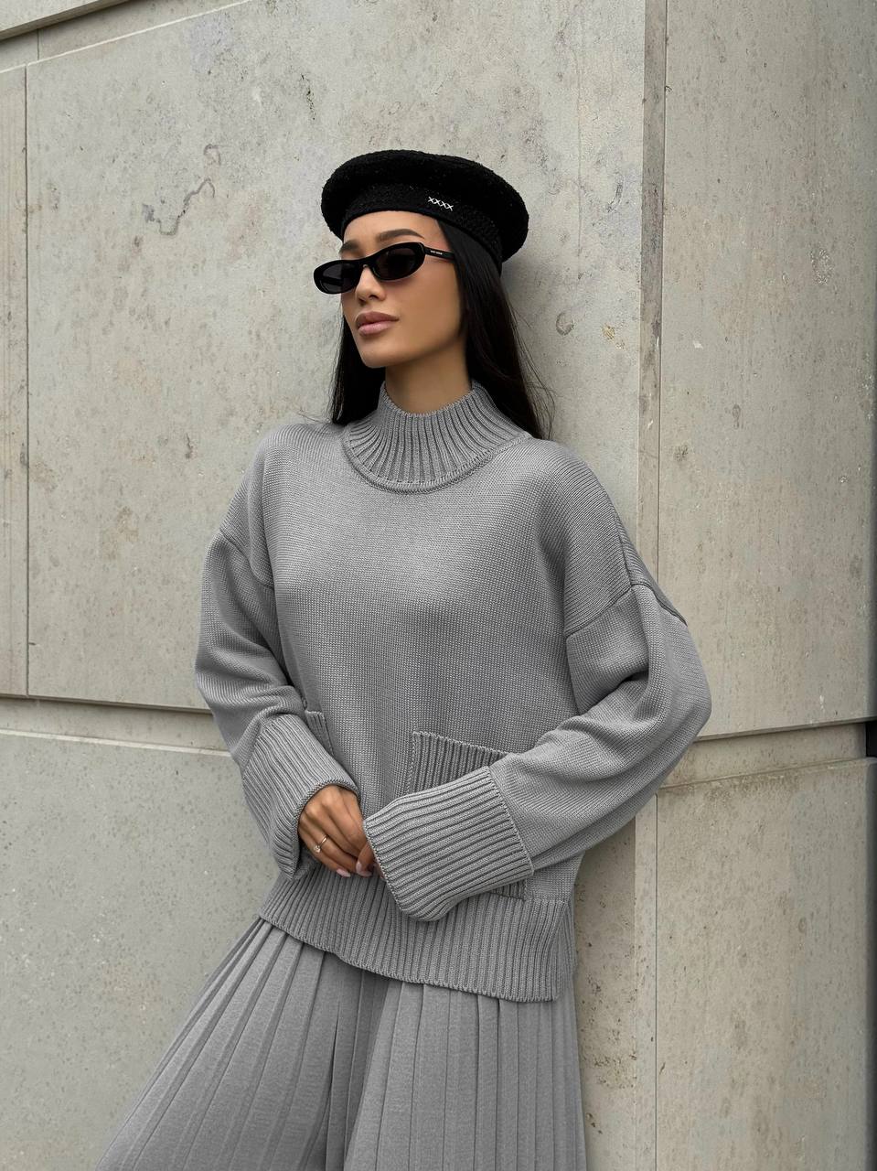 Person wearing a gray sweater and skirt with a black beret against a stone wall.