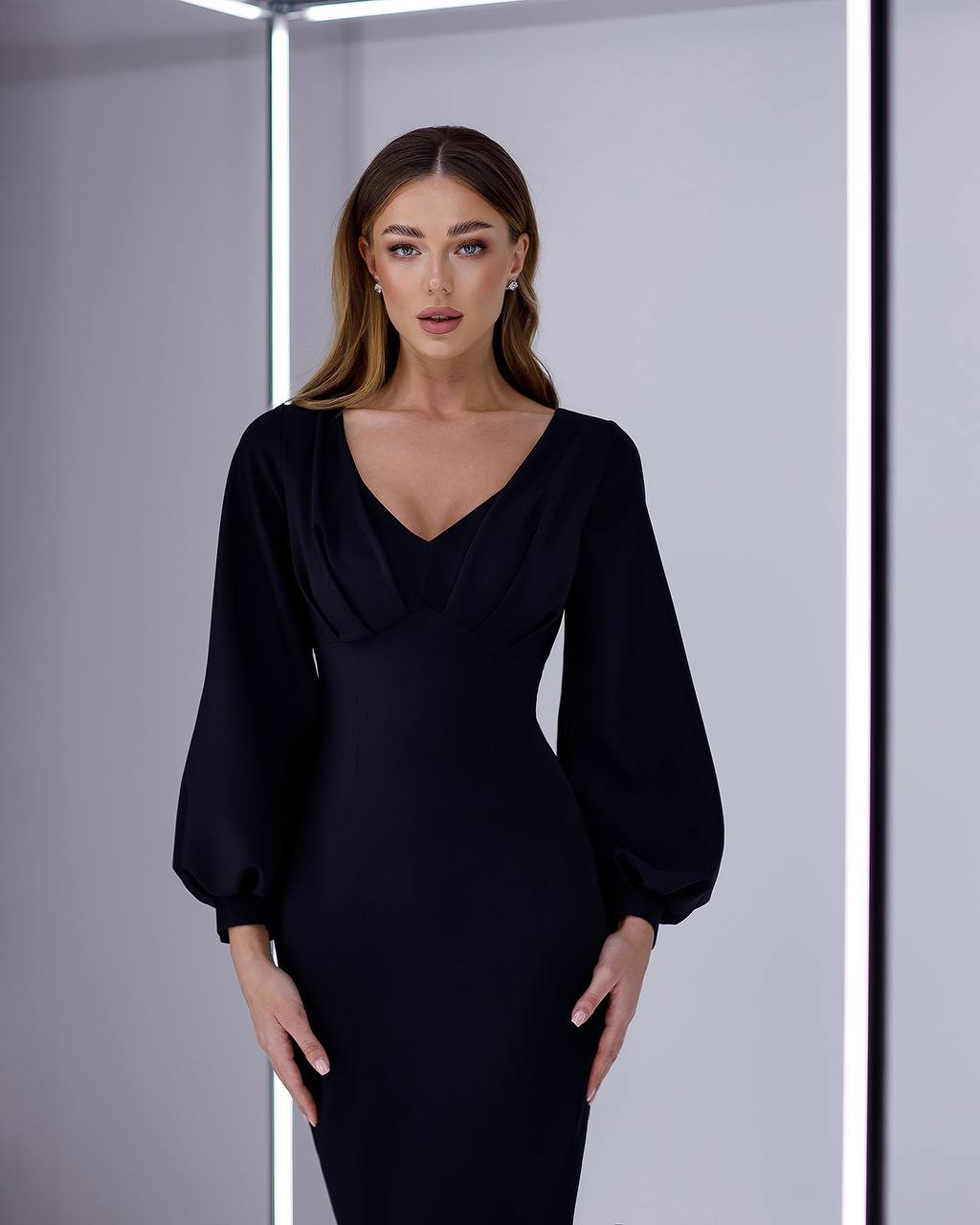Woman wearing a black dress with long sleeves against a neutral background