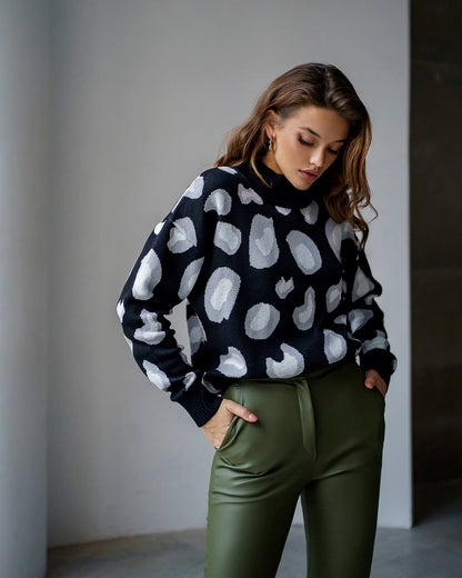 Woman wearing a black sweater with white polka dots and green pants against a neutral background