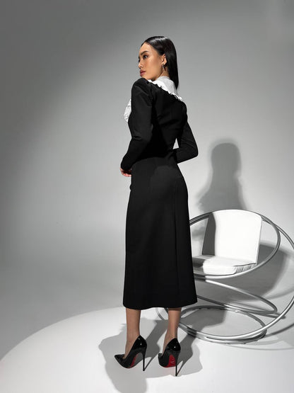 Woman in a black dress with white collar standing in a minimalistic setting.