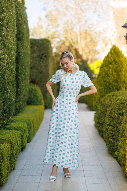 Woman in a floral dress standing in a garden with manicured hedges.