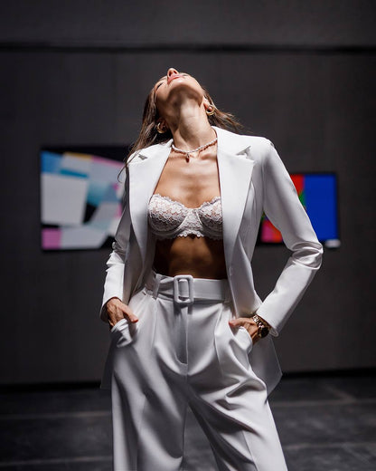 Person wearing a white suit with a bralette against a dark background