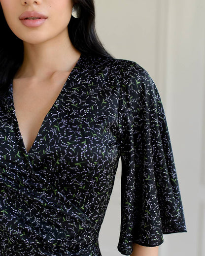 Woman wearing a black patterned dress against a neutral background