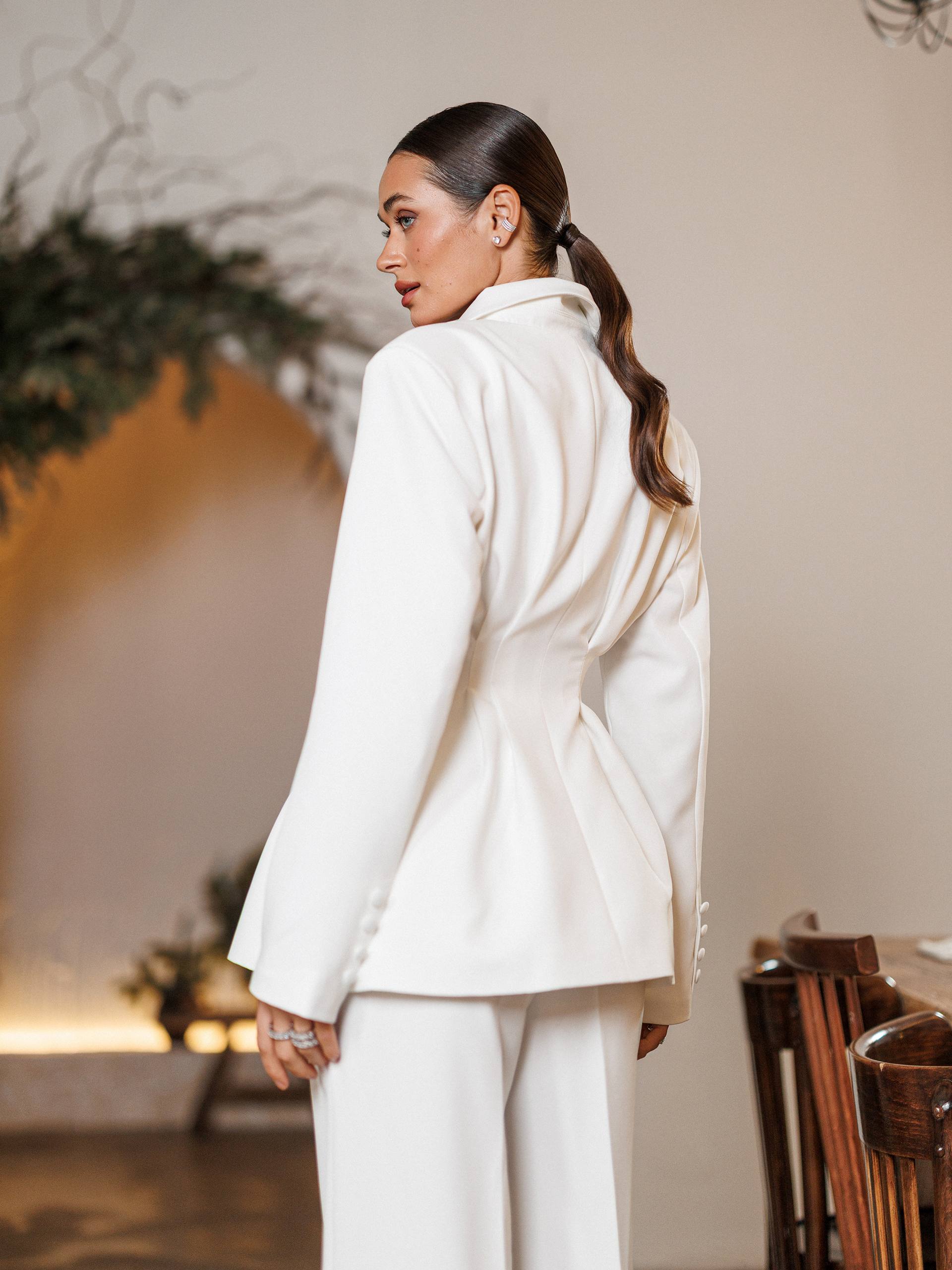 Woman in a white suit standing in an indoor setting with a neutral background