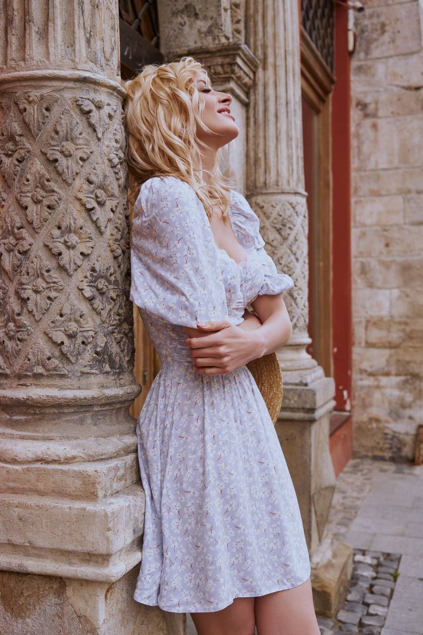 Woman in a white dress standing against an ornate stone wall.