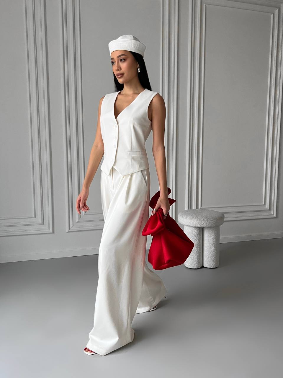 Woman in a white outfit holding a red bag in a minimalistic setting