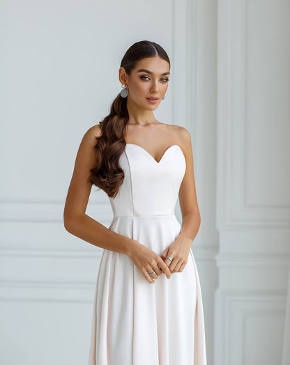 Woman wearing a white strapless dress against a plain background