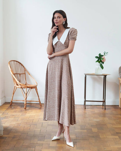 Woman in a patterned dress standing in a room with wooden flooring and minimal decor.