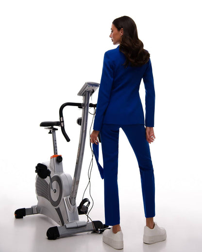 Woman in a blue suit standing next to an exercise bike on a white background