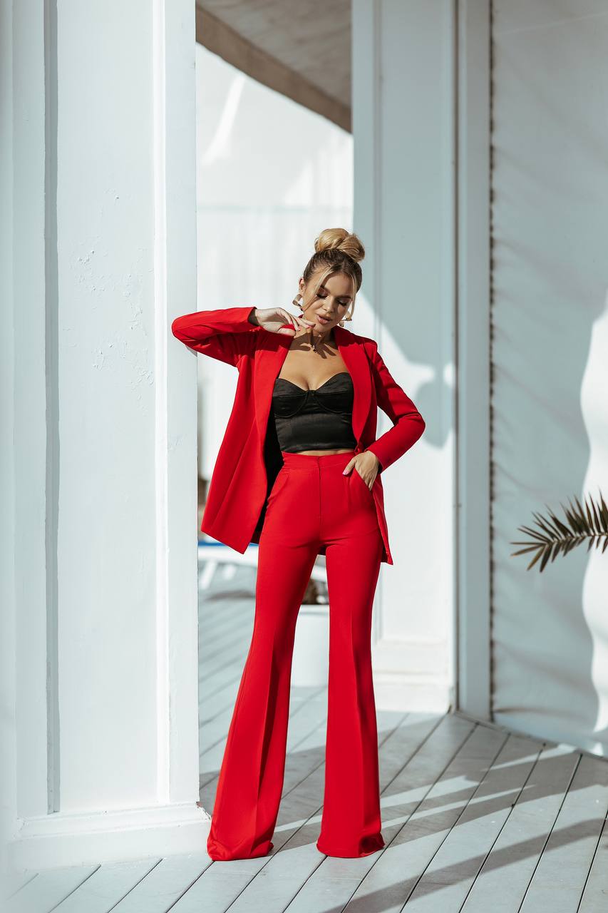Woman in a red suit standing in a bright room with white walls and wooden floor.