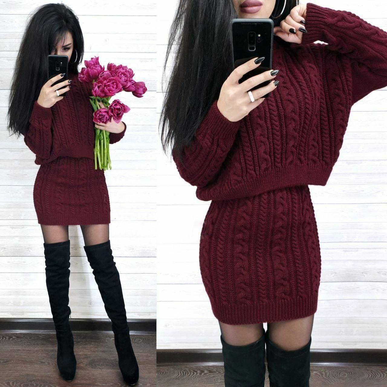 Woman wearing a burgundy cable knit sweater dress with black knee-high boots, holding pink flowers.