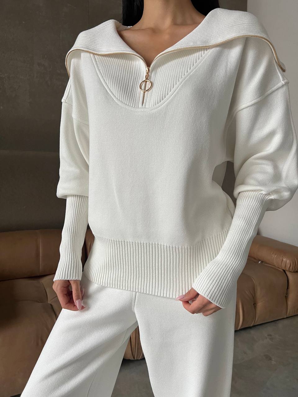 Person wearing a white sweater with a zipper detail in a neutral setting