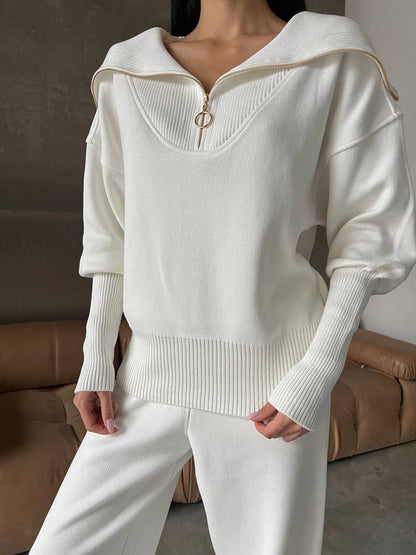 Person wearing a white sweater with a zipper detail in a neutral setting