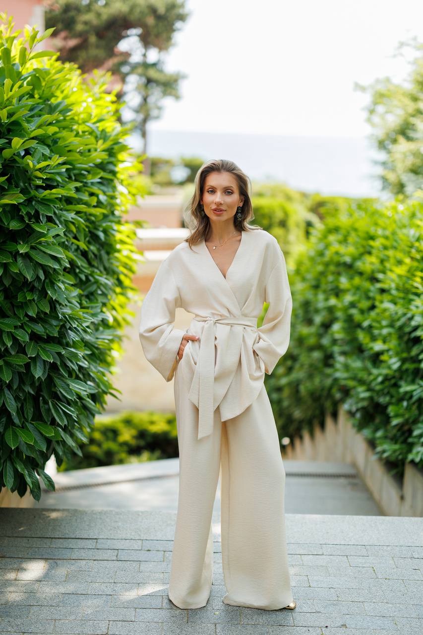 Woman in a beige outfit standing outdoors with greenery around