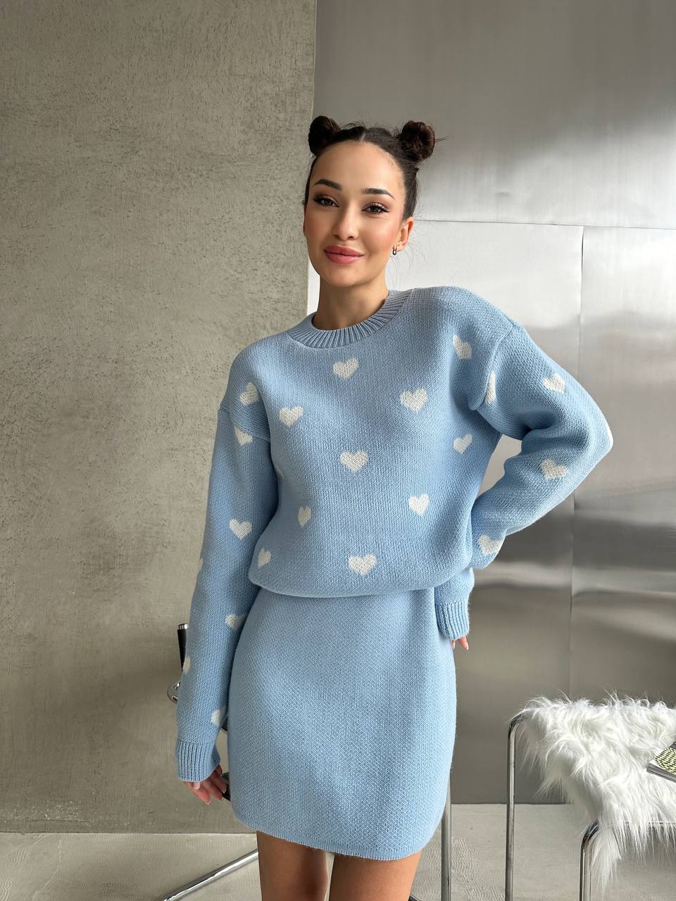 Woman wearing a light blue sweater and skirt set with heart patterns indoors.
