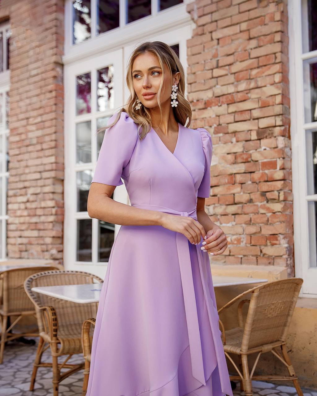 Woman in a purple dress standing outdoors with a brick building and tables in the background