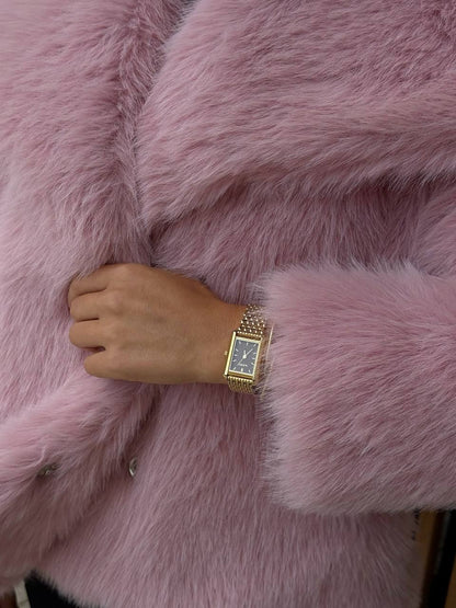 Hand wearing a gold watch on a pink fur surface