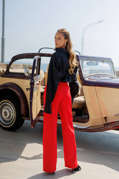 Woman in red pants and black top standing next to a vintage car