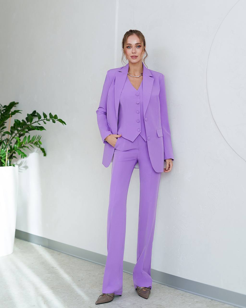 Woman wearing a purple suit standing in an indoor setting with a plant.