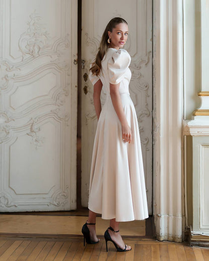Woman in a white dress standing in an elegant room with decorative walls.
