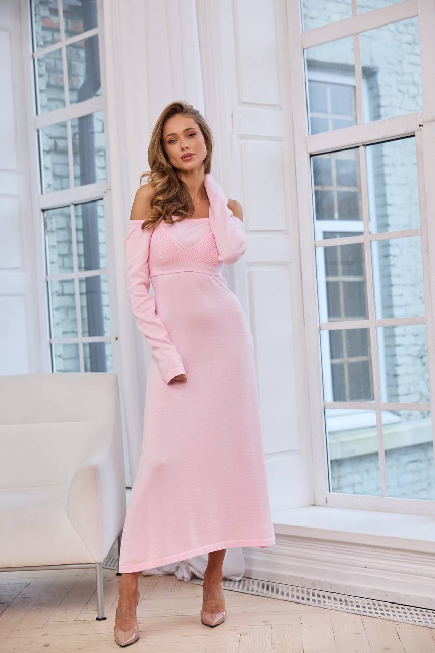 Woman wearing a pink dress standing in a room with large windows.