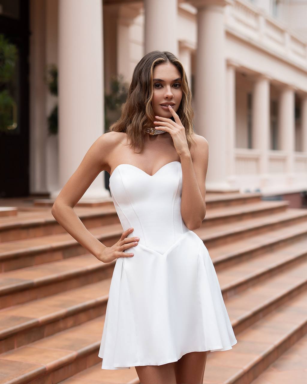 Woman in a white dress standing on steps with classical architecture in the background