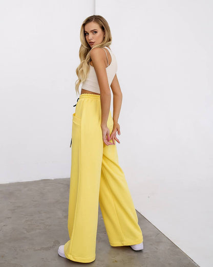 Woman wearing a white top and yellow pants against a plain background