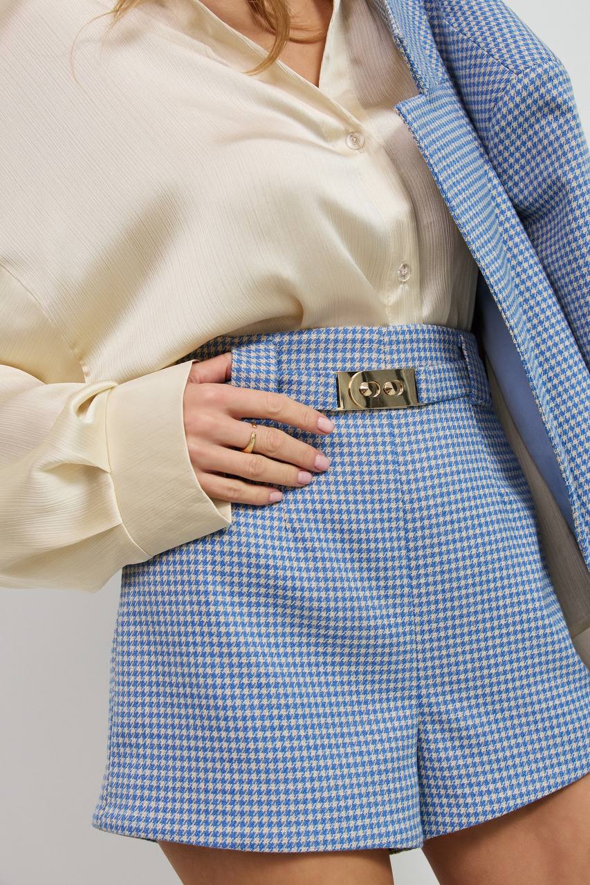 Person wearing a blue checkered skirt with a beige top and blue jacket.