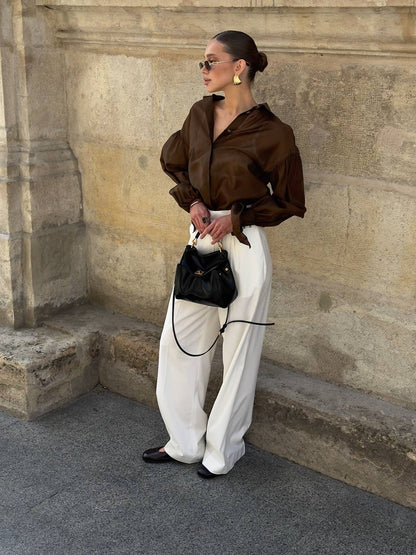 Woman in brown shirt and white pants standing against a stone wall.