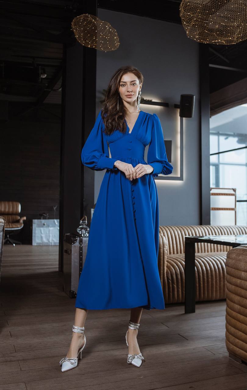 Woman in a blue dress standing in an indoor setting with modern decor.