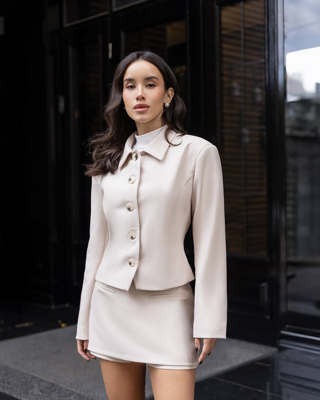 Woman wearing a beige suit standing in front of a building entrance.