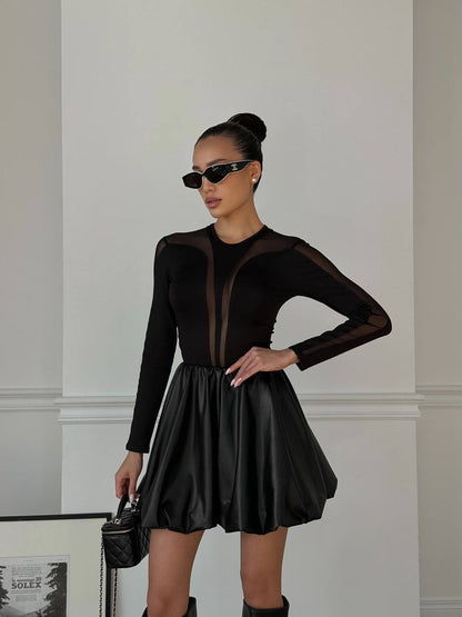 Woman wearing a black dress with sheer panels against a neutral wall.