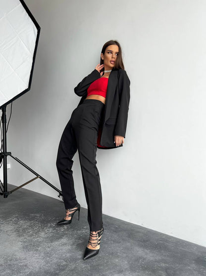 Woman in a black blazer and red top posing in a studio setting.