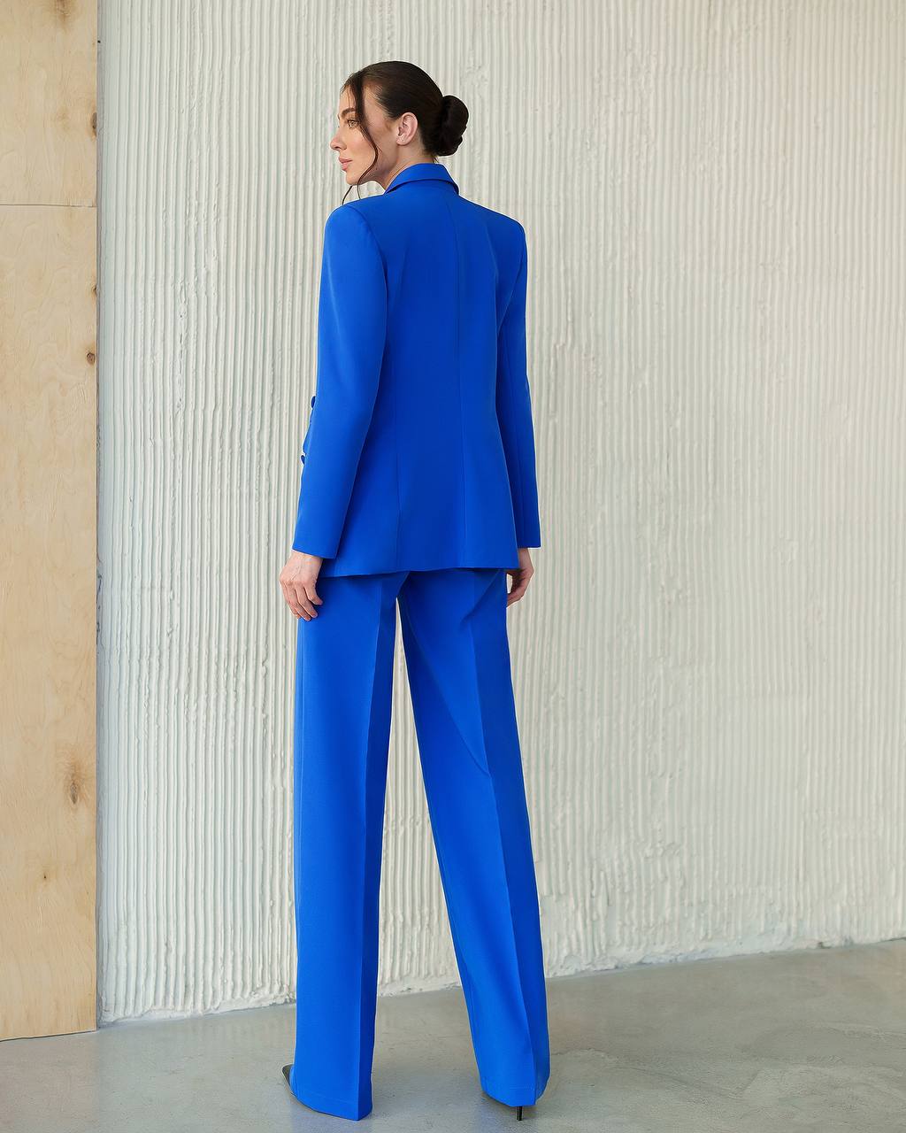 Woman wearing a blue suit standing against a textured wall.
