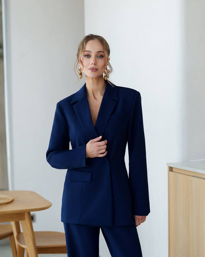 Woman wearing a navy blue suit standing indoors with a neutral background
